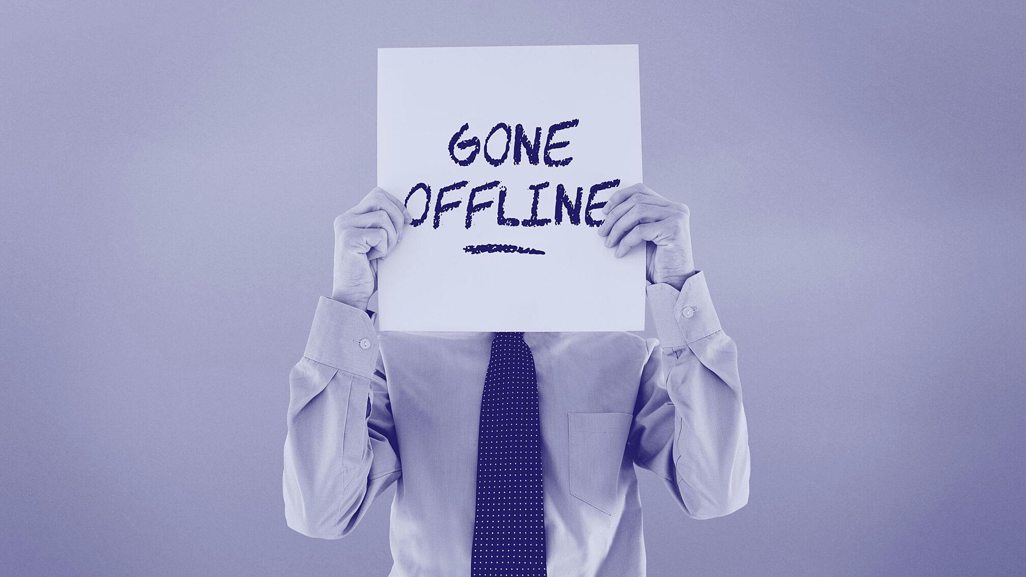 Business executive holding sign in front of face that says gone offline.